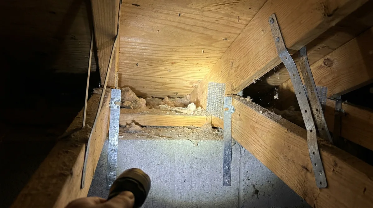 Galvanized hurricane straps connecting wooden roof trusses to the top plate of a concrete block wall, photographed inside a Florida attic